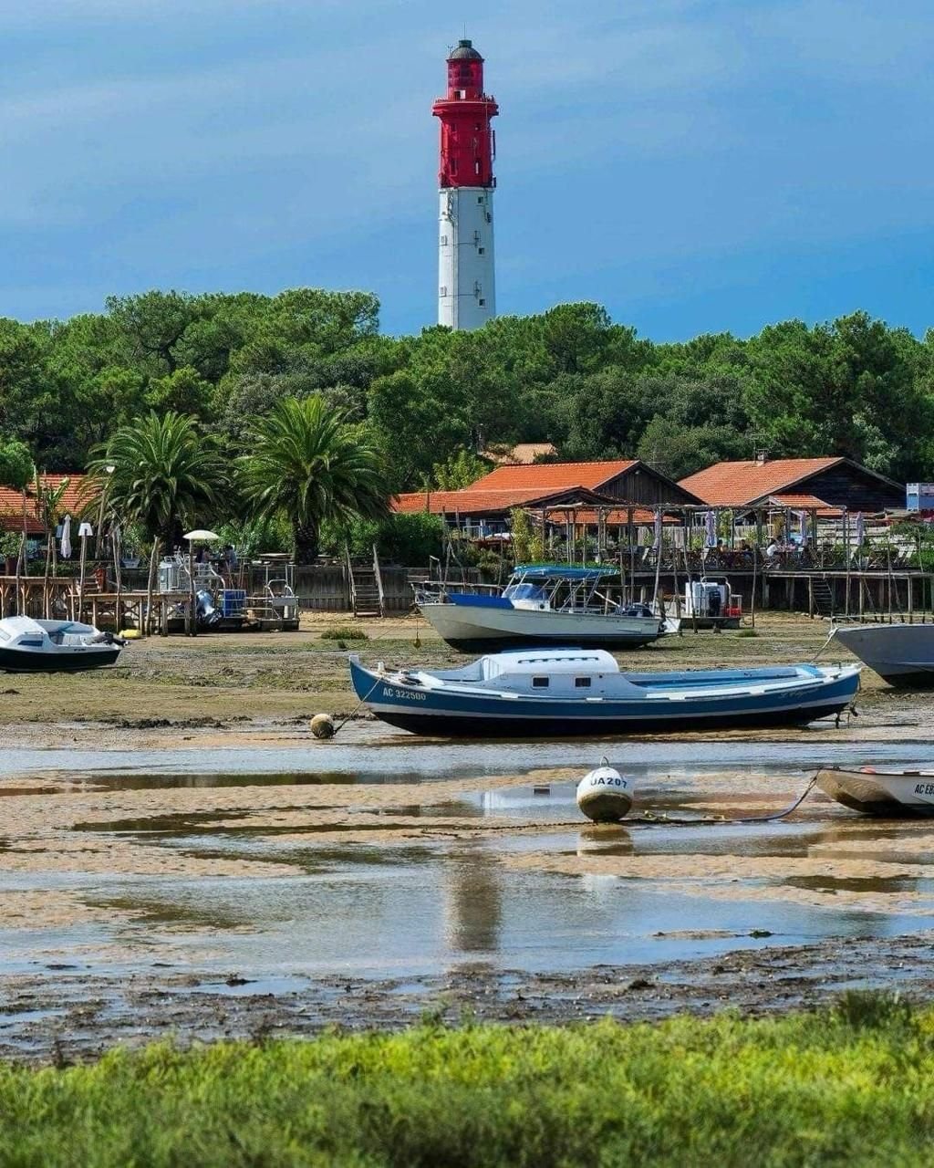 Le phare rouge et blanc du Cap Ferret au-dessus des cabanes et des bateaux à marée basse